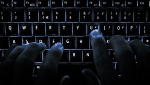 A backlit laptop computer keyboard. Most fingers are on the "home" keys for touch-typing; the 'U' key is being pressed.