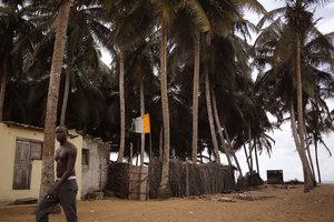 A man, left, passes a home stead, with a Ivory Coast national flag, center, seen at a fishing village renowned as a tourist hot spot visited by French and other tourist yearly in Grand Bassam, Ivory Coast, Tuesday, Oct. 27, 2015.