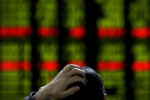 A man scratches his head as he checks the stock prices on an electronic board at a brokerage house in Beijing, Tuesday, ...