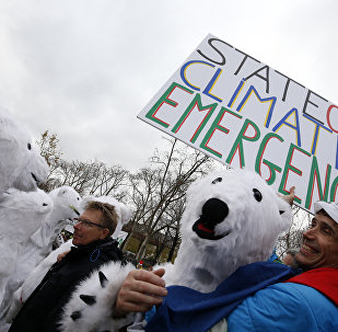 Jean-Baptiste Redde aka Voltuan holds a banner reading State of climate emergency next to demonstrators dressed-up as polar bears during a rally called by several Non Governmental Organisations (NGO) to form a human chain on the Champs de Mars near the Eiffel Tower in Paris on December 12, 2015 on the sidelines of the COP21, the UN conference on global warming.