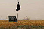 Smoke rises in the distance behind an Islamic State (IS) group flag and banner