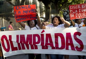 FILE - In this Aug. 5, 2015, file photo, people protest against the 2016 Olympic Games while they hold posters that read in Portuguese "I am a street vendor and my family starves" and "Attorney acts and the police steals," in front of the headquarters of the Olympic Organizing Committee in Rio de Janeiro, Brazil. Brazil’s economic and political crisis has relegated Rio de Janeiro's Olympic preparations to an afterthought.