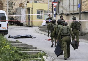 Israeli soldiers stand near the body a Palestinian who was shot while laying wounded on the ground after a stabbing attack in Hebron, West Bank, Thursday, March 24, 2016.