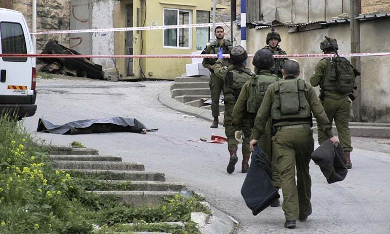 Israeli soldiers stand near the body a Palestinian who was shot while laying wounded on the ground after a stabbing attack in Hebron, West Bank, Thursday, March 24, 2016. ─ AP