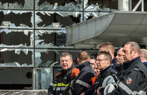 Firefighters and first responders stand next to blown out windows at Zaventem Airport in Brussels on Wednesday, March 23, 2016.