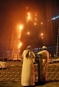 Two Emirati officials as a fire spreads up the side of the watch a high-rise building in Ajman, United Arab Emirates, early Tuesday, March 29, 2016. Police