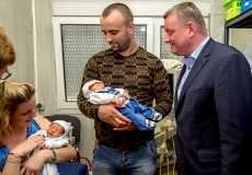 Foto: Bundesgesundheitsminister Gröhe mit der saarländischen Ministerpräsidentin Annegret Kramp-Karrenbauer und sowie einem Paar; die Frau und der Mann halten jeweils ein Baby in ihren Armen (Bildquelle: BMG/Silz)