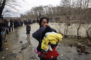 File - Woman holding her baby cries after crossing the river along with other migrants, north of Idomeni, Greece, attempting to reach Macedonia on a route that would bypass the border fence, Monday, March 14, 2016.