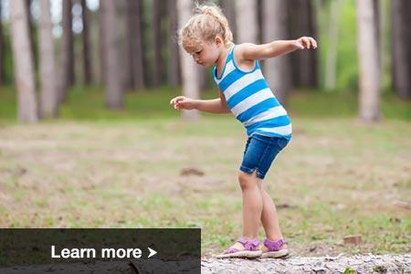 A young girl walks across a fallen log. Click to learn more about dizziness and balance problems for U.S. children.