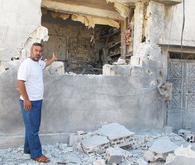 File - A resident of Homs, Syria, shows UN observers a building heavily damaged in the renewed rounds of shelling which rained down on the city this weekend, 11 June, 2012.