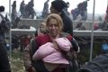 A woman carries a child on the Greek side of the border as they run away after Macedonian police fired tear gas at a ...