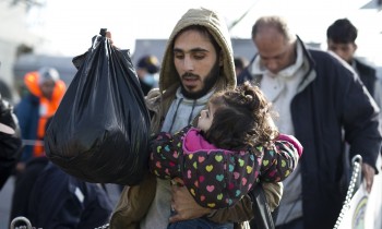 A Syrian man carries a child as they disembark from a Greek navy vessel after a rescue operation near the shores of Lesbos  (AP Photo/Petros Giannakouris)