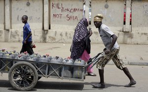 A man pushes a cart filled with water bottles past a sign reading "Kill Boko Haram not shia" in Kano, Nigeria, Friday, April 8, 2016.