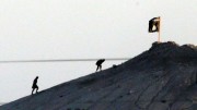 In this image shot with an extreme telephoto lens and through haze from the outskirts of Suruc at the Turkey-Syria border, militants with the Islamic State group are seen after placing their group's flag on a hilltop at the eastern side of the town of Kobani, Syria, where fighting had been intensified between Syrian Kurds and the militants of Islamic State group, Monday, Oct. 6, 2014. (AP Photo/Lefteris Pitarakis)