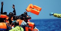 A Belgian nav.y sailor passes life vests to migrants sitting in a rubber boat as they approach the Belgian Navy Vessel Godetia during a search and rescue mission in the Mediterranean Eea off the Libyan coasts, Tuesday, June 23, 2015