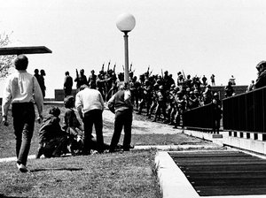 A group of youths cluster around a wounded person as Ohio National Guardsmen, wearing gas masks, hold their weapons in background on Kent State University campus in Kent, Ohio, Monday, May 4, 1970.