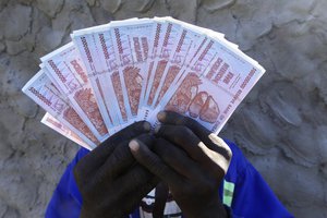 A man holds a handful of 5 Billion Zimbabwean dollar notes, in Harare, Friday, June, 12, 2015.