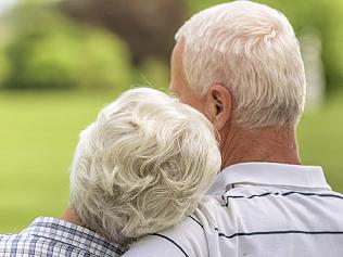 Senior woman resting head on shoulder of senior man while sitting on bench in park together.