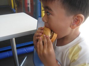 File - A young boy eats a hamburger in a fast food restaurant.