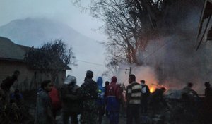 Villagers and rescuers stand near a burning tree after it was hit by pyroclastic flows from the eruption of Mount Sinabung, background, in Gamber, North Sumatra, Indonesia