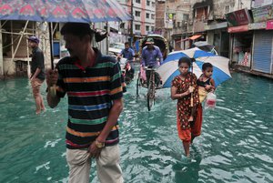 Bangladeshi people walk through a waterlogged street after heavy rainfall in Dhaka, Bangladesh