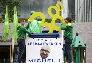 Union members put a sign which reads '38 hours' into a dumpster above a poster of Belgian Prime Minister Charles Michel which reads 'Social Dismantling' during a demonstration in Brussels on Tuesday, May 24, 2016.