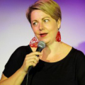 Middle aged white woman speaking into hand-held microphone.