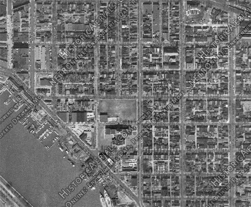 It's an aerial view photo of a neighborhood filled with little rows of houses and shops, lots of green space, small roads criss-crossing.