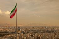 Iran flag waving in the wind above the skyline of Tehran lit by the orange glow of sunset.