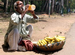 File - An old thirsty man sells bananas on the road side, while drinking water, on a very hot day, May 1, 2016 in Jammu, India.