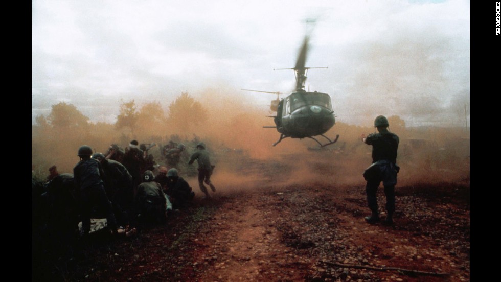 Tim Page photographed a U.S. helicopter taking off from a clearing near Du Co SF camp in Vietnam in 1965. Wounded soldiers crouch  in the dust of the departing helicopter. The military convoy was on its way to relieve the camp when it was ambushed.