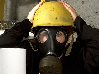Woman dressed in gas mask and hard hat hiding in the basement with stockpiled goods
