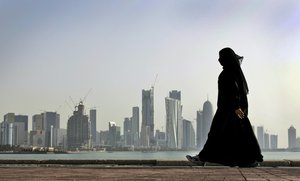 FILE- In this May 14, 2010 file photo, a Qatari woman walks in front of the city skyline in Doha, Qatar.