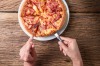 Cutting a delicious Italian pizza with cheese, mushrooms, artichokes and tomatoes with help of knife and fork