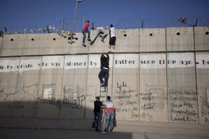 In this Friday, June 19, 2015 file photo young Palestinians use a ladder to climb over the separation barrier with Israel in Al-Ram, north of Jerusalem. Israel has built several walls and fences, including its West Bank separation barrier, which is to reach 450 miles (700 kilometers) when complete.