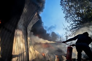 A resident attempts to extinguish a fire in a burning storeroom on church property as angry residents refused to accept the replacement of Pretoria's mayoral candidate in Atteridgeville, Pretoria, South Africa, Tuesday June 21, 2016.