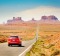 Subject: Tourists in a red car traveling in the American Southwest, driving downhill on a straight length of highway ...