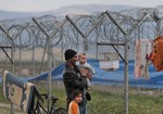 Syrian refugee Abdullah Koca, 43, who fled Syria four-years ago and had been living at a refugee camp for Syrian refugees in Islahiye, Gaziantep province, southeastern Turkey, holds his six-month-old son Ibrahim and his daughter Hadiyeh, 6, as they check the family pet bird suspended in a cage at the barbed-wired fence of the camp, Wednesday, March 16, 2016.