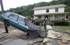 Jay Bennett, left, and step-son Easton Phillips survey the damage to a neighbors car in front of their home damaged by floodwaters as the cleanup begins from severe flooding in White Sulphur Springs, W. Va., Friday, June 24, 2016.