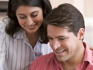 Couple in kitchen with paperwork using laptop smiling