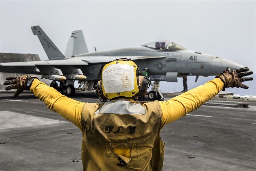 Navy Petty Officer 3rd Class Raimon Hubbard directs an F/A-18E Super Hornet on the flight deck of the aircraft carrier USS Harry S. Truman