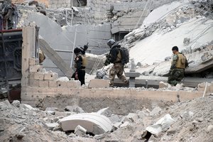 Iraqi security forces, supported by U.S.-led coalition airstrikes, advance their position through damaged buildings towards central Ramadi, 70 miles (115 kilometers) west of Baghdad, Iraq, Thursday, Dec. 24, 2015. The advance of government forces in the Islamic State-held city of Ramadi is being hampered by suicide bombers, snipers and booby traps.