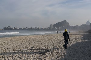 A construction worker of the Olympic beach volleyball venue observes a dismembered human foot covered with black plastic after it was found in front of the venue in Copacabana beach in Rio de Janeiro, Brazil, Wednesday, June 29, 2016.