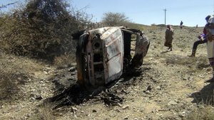 File - People gather near a destroyed car that was carrying militants in the Sawmaa area of al-Bayda province, Yemen, Saturday, April 19, 2014. A Yemeni military official says an American drone strike has killed nine suspected al-Qaida militants and inadvertently killed and wounded some civilians.