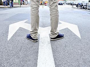 Arrows painted on asphalt. Young man standing hesitating to make a decision.