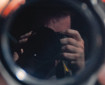 Photograph taken of the photographers reflection in a mirror, mostly what we see is the camera with some fingers and some forehead