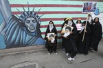 Female Iranian school girls stand in front of a satirized drawing of the Statue of Liberty, painted on the wall of the former US Embassy in Tehran, Iran