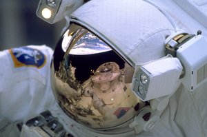 The Space Shuttle Discovery's Cargo Bay and Crew Module, and the Earth's horizon are reflected in the helmet visor of one of the space walking astronauts on STS-103. Astronauts Steven L. Smith, John M. Grunsfeld, C. Michael Foale and Claude Nicollier participated in three days of extravehicular activity on the NASA's third servicing visit to the Hubble Space Telescope (HST).