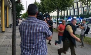 Armed police move past onlooking media responding to a shooting at a shopping center in Munich, Germany, Friday July 22, 2016.