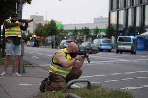 Police officers point their weapons outside the Olympia mall in Munich, southern Germany, Friday, July 22, 2016 after several people have been killed in a shooting